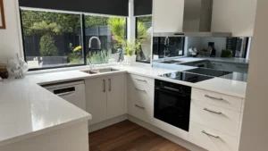 Modern custom-built U-shaped kitchen renovation featuring white cabinetry with silver handles, engineered stone benchtops, and a mirrored splashback installed by Hamilton Kitchens