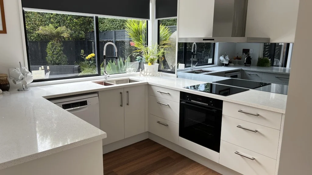 Modern custom-built U-shaped kitchen renovation featuring white cabinetry with silver handles, engineered stone benchtops, and a mirrored splashback installed by Hamilton Kitchens