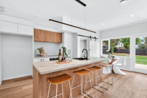 Scandi industrial style kitchen showing a custom timber island bench with a concrete-look top, modern wooden bar stools, and matte black fixtures by Hamilton Kitchens