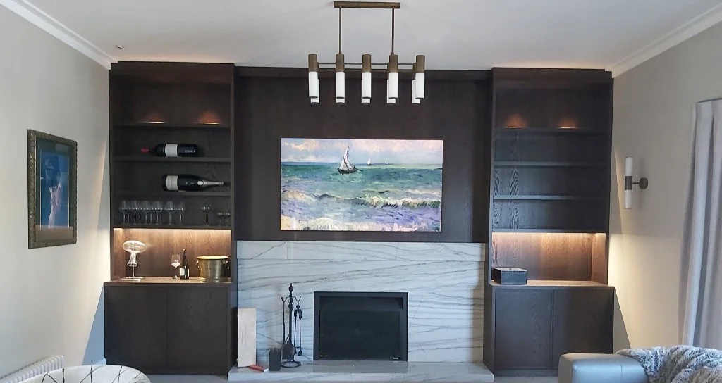 Custom dark wood living room built-ins flanking a marble fireplace with a hidden TV and integrated bar shelves.